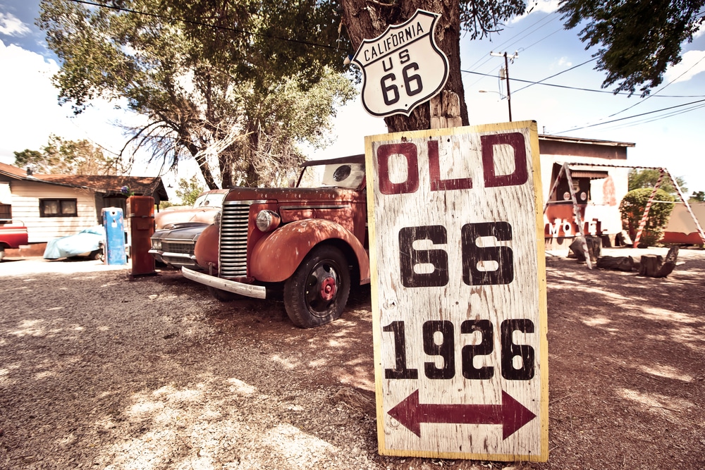 Old,Route,66,Signs,With,Rusty,Cars,In,Background